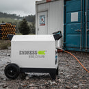 Weißer fahrbarer Energiespeicher 'ESS D 11/8' der Firma ENDRESS auf einer Baustelle mit zwei Tragegriffen seitlich an der Oberseite, verschiedene Steckdosen an der Seite mit eingestecktem Kabel, zwei Standfüße, zwei Räder und einem ausziehbaren Handgriff an der Unterseite.
