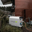 Weißer fahrbarer Energiespeicher 'ESS D 11/8' der Firma ENDRESS im Gras vor einem Foodtruck mit zwei Tragegriffen seitlich an der Oberseite, verschiedene Steckdosen an der Seite mit eingestecktem Kabel und zwei Standfüße und einem ausziehbaren Handgriff an der Unterseite.